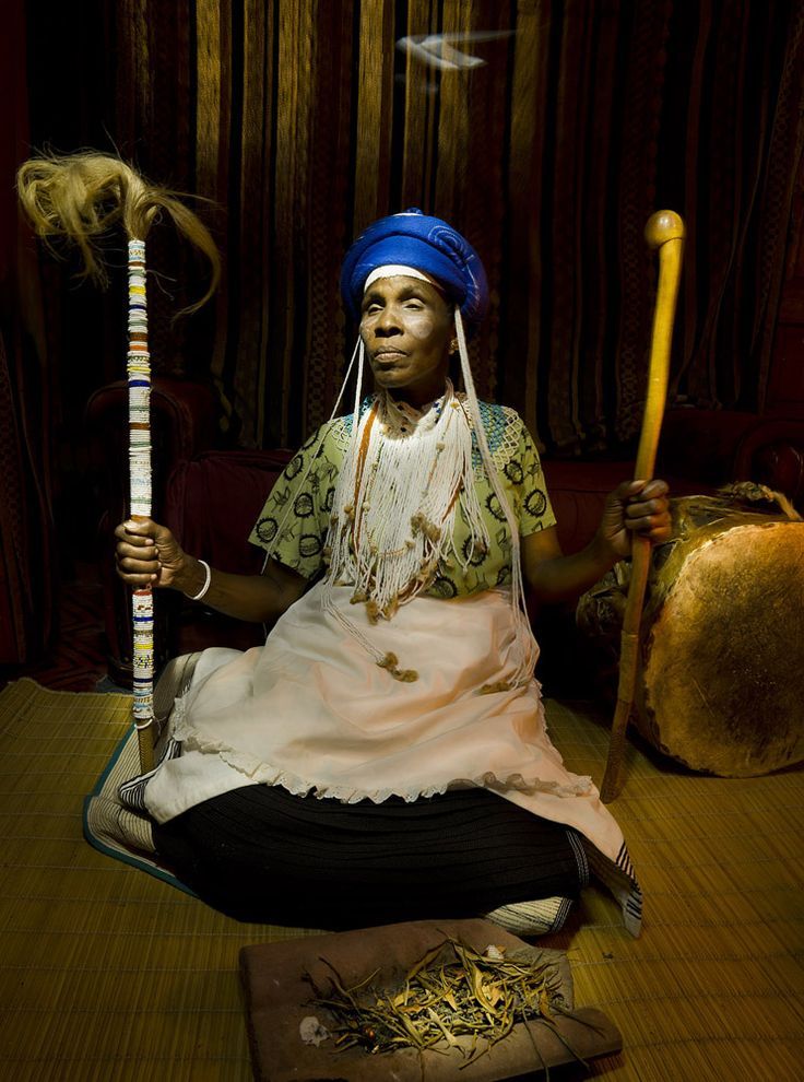Mama Mwangaza seated in traditional regalia, holding her ritual staff